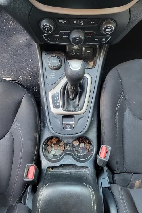 Jeep center console and cupholders with coins and debris before detailing