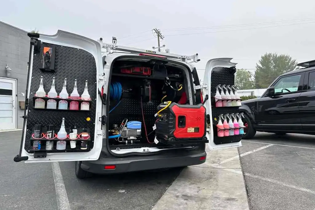 Open mobile detailing van organized with pressure washer, hoses, and labeled bottles