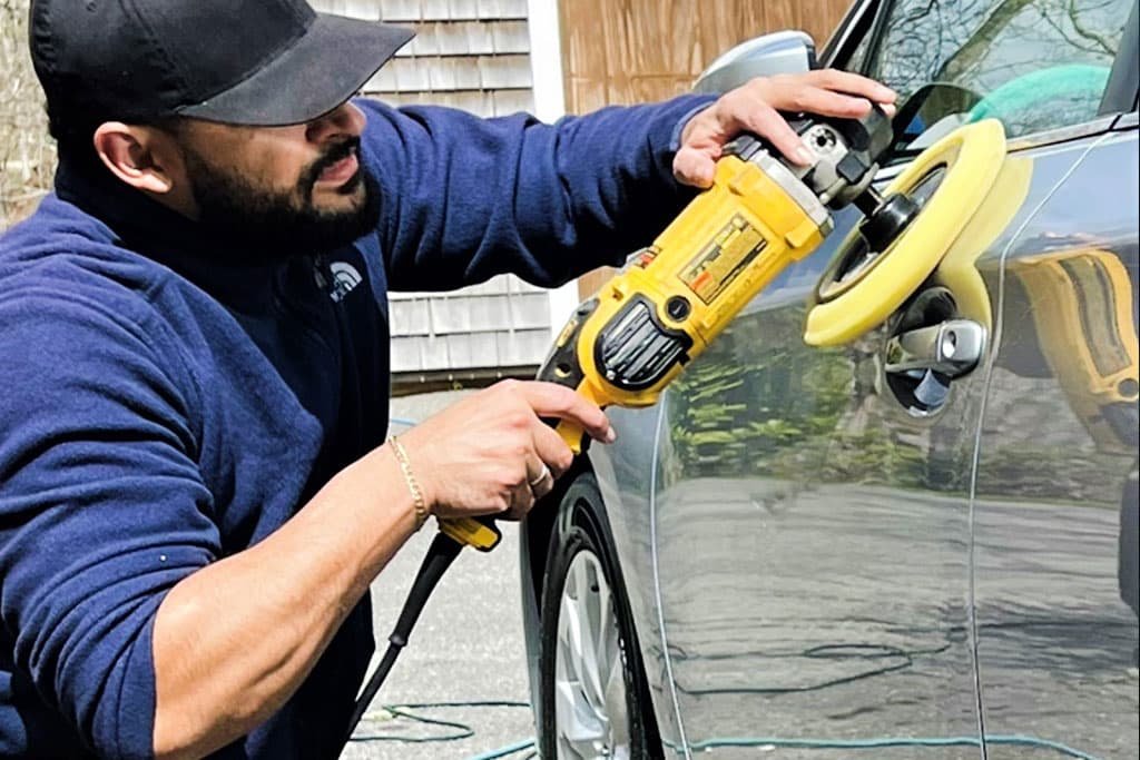Detailer using a dual-action polisher on a dark vehicle door