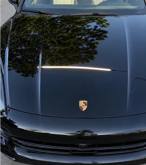 Same black Porsche hood with reduced swirl visibility after paint correction