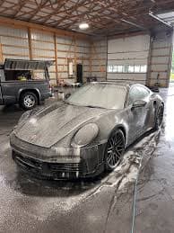 Porsche covered in cleaning foam during a controlled pre-wash inside a service bay