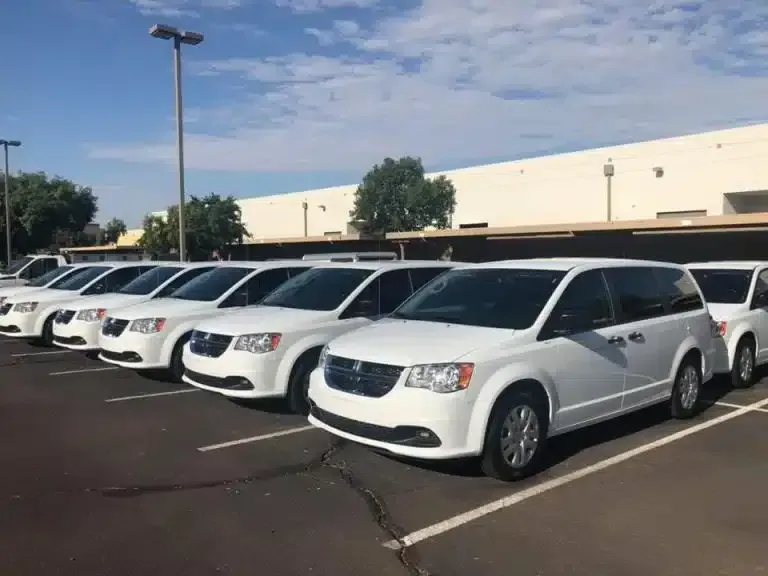 Row of white passenger vans parked at a commercial facility